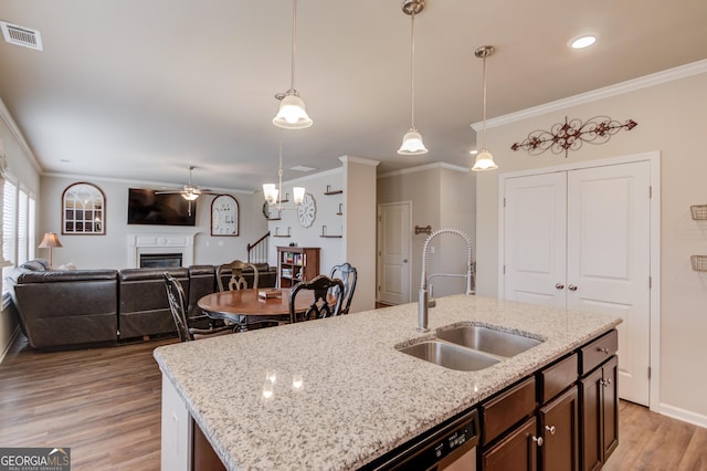 kitchen with crown molding, sink, hanging light fixtures, and an island with sink