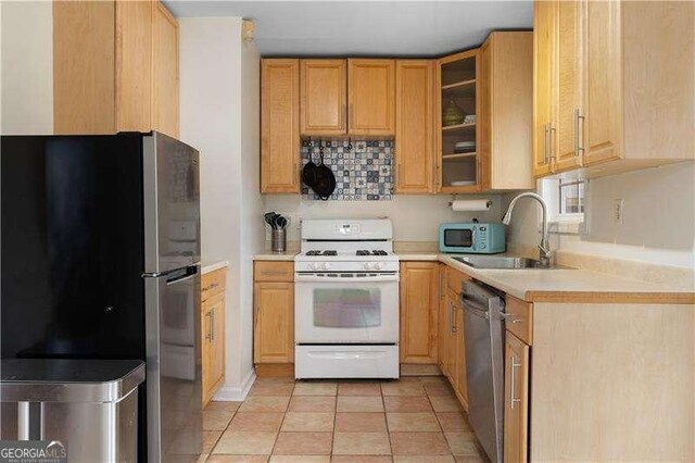 kitchen with stainless steel appliances, sink, light tile patterned floors, and light brown cabinetry