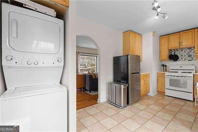 kitchen featuring stainless steel fridge, decorative backsplash, stacked washer and dryer, white range with gas stovetop, and light tile patterned floors