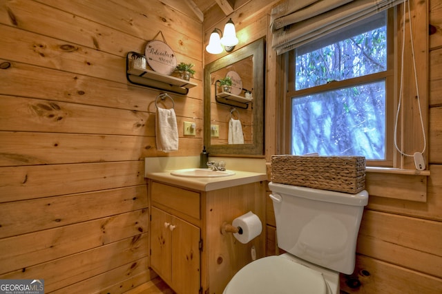 bathroom featuring toilet, vanity, and wood walls