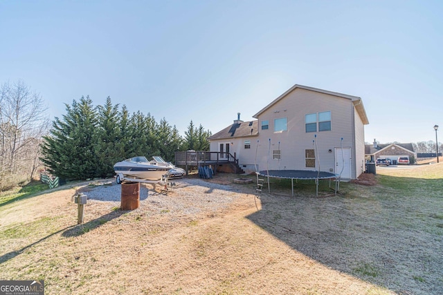 rear view of property featuring a wooden deck, a trampoline, and a lawn