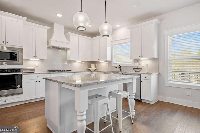 kitchen with white cabinetry, a kitchen island, stainless steel appliances, and premium range hood