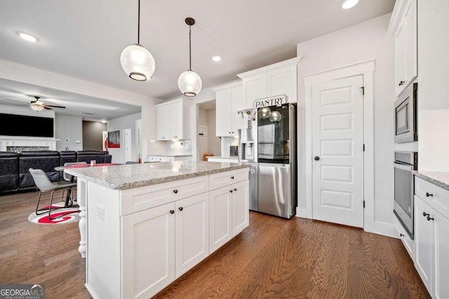 kitchen with a center island, appliances with stainless steel finishes, pendant lighting, light stone countertops, and white cabinets