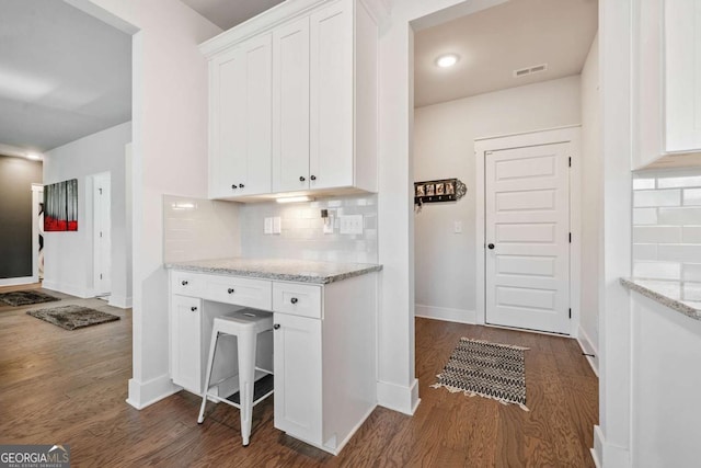 kitchen with light stone countertops, dark wood-type flooring, white cabinets, and decorative backsplash