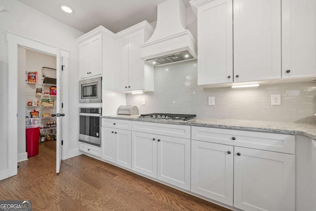 kitchen featuring appliances with stainless steel finishes, tasteful backsplash, custom range hood, white cabinets, and light wood-type flooring