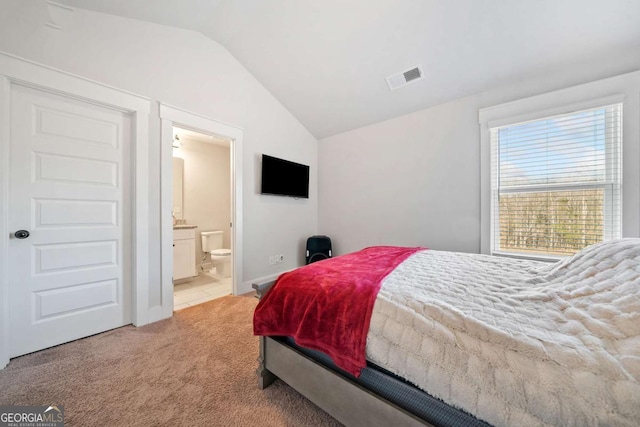 bedroom with lofted ceiling, light carpet, and ensuite bath