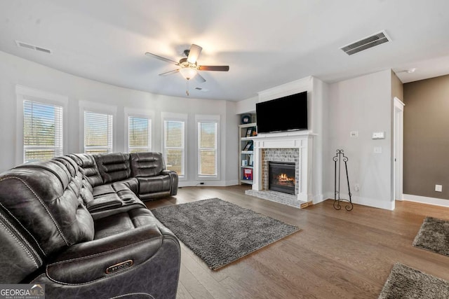 living room with a brick fireplace, built in features, ceiling fan, and light hardwood / wood-style flooring