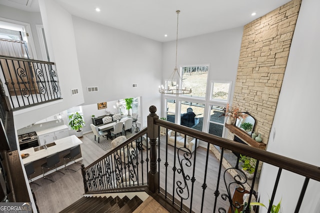 stairway featuring an inviting chandelier, a towering ceiling, and wood-type flooring