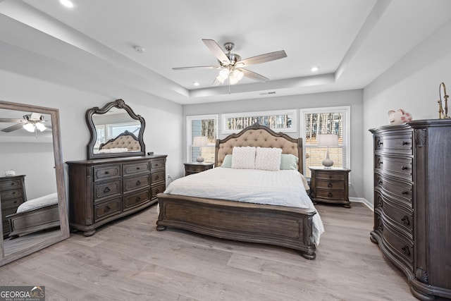 bedroom with multiple windows, a tray ceiling, and light hardwood / wood-style flooring