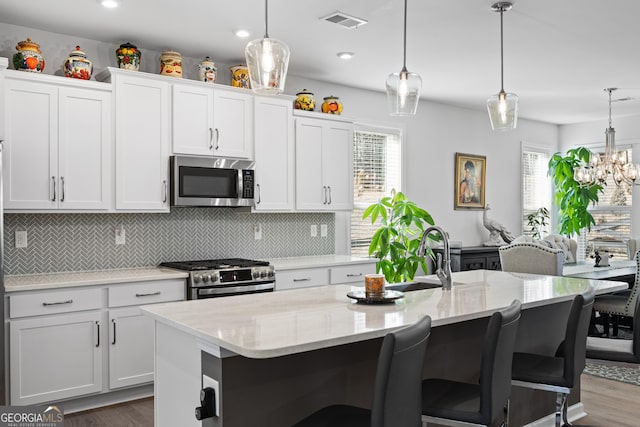 kitchen with stainless steel appliances, white cabinetry, a kitchen island with sink, and pendant lighting