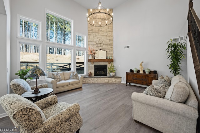 living room with a high ceiling, wood-type flooring, a stone fireplace, and a chandelier