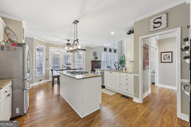 kitchen featuring a kitchen island, appliances with stainless steel finishes, pendant lighting, white cabinets, and light stone counters