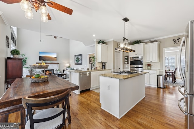 kitchen featuring kitchen peninsula, pendant lighting, stainless steel appliances, light stone countertops, and white cabinets