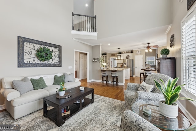 living room with a towering ceiling, wood-type flooring, and ceiling fan