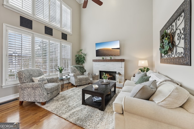 living room with hardwood / wood-style floors, ceiling fan, a brick fireplace, and a high ceiling