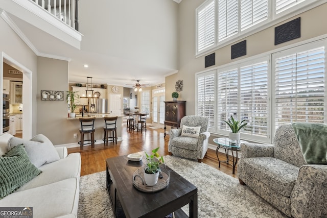 living room with crown molding, a towering ceiling, hardwood / wood-style floors, and ceiling fan