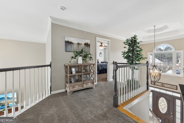 corridor featuring ornamental molding, a chandelier, a raised ceiling, and carpet