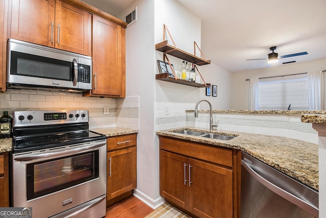 kitchen with light stone counters, appliances with stainless steel finishes, sink, and light hardwood / wood-style flooring