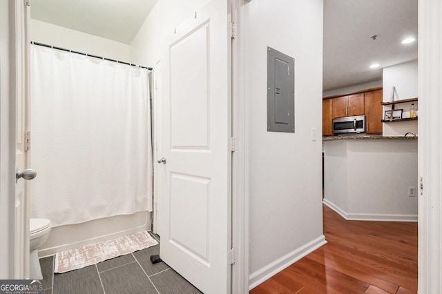 bathroom with shower / bath combination with curtain, hardwood / wood-style floors, electric panel, and toilet