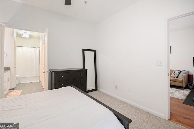 bedroom with ceiling fan, light colored carpet, and connected bathroom