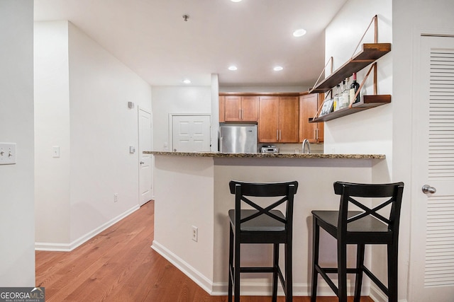 kitchen with stone countertops, stainless steel refrigerator, light hardwood / wood-style floors, a kitchen bar, and kitchen peninsula