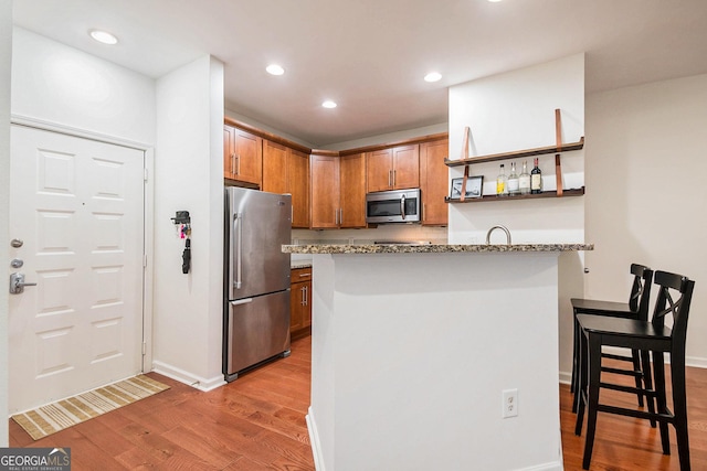 kitchen with backsplash, light stone counters, kitchen peninsula, stainless steel appliances, and light hardwood / wood-style floors