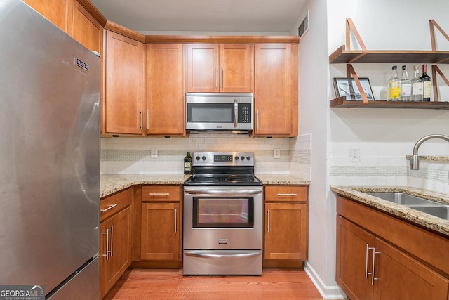 kitchen featuring sink, light stone counters, light wood-type flooring, appliances with stainless steel finishes, and decorative backsplash