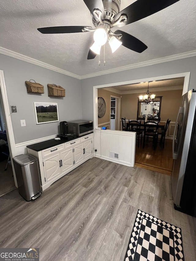 interior space featuring light hardwood / wood-style flooring, stainless steel refrigerator, ornamental molding, a textured ceiling, and white cabinets