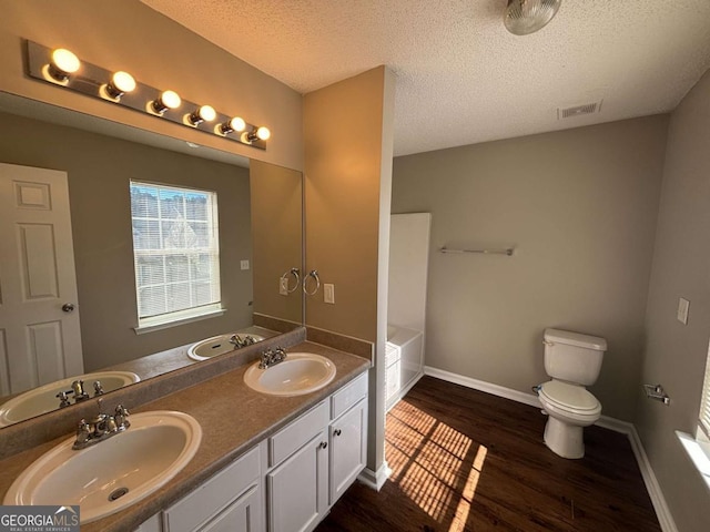 bathroom featuring toilet, wood-type flooring, a textured ceiling, vanity, and a bath