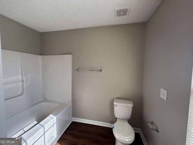 bathroom with a bathtub, a textured ceiling, wood-type flooring, and toilet