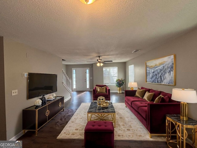 living room with dark wood-type flooring, ceiling fan, and a textured ceiling