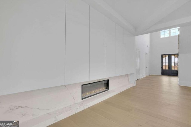 unfurnished living room featuring high vaulted ceiling, light hardwood / wood-style floors, and french doors