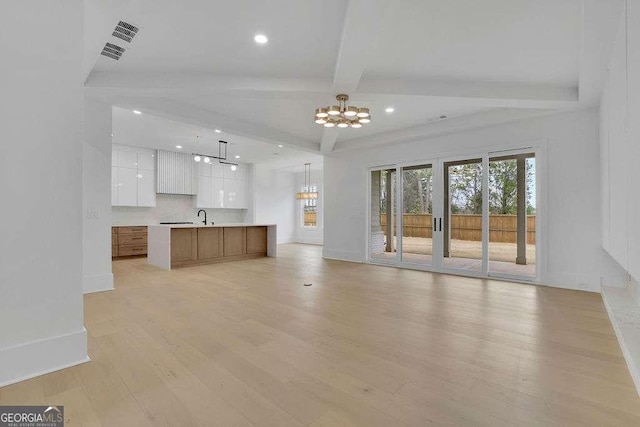 unfurnished living room featuring beamed ceiling, sink, light wood-type flooring, and a notable chandelier