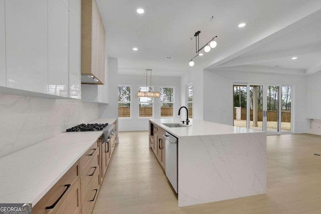 kitchen featuring pendant lighting, sink, a large island, stainless steel appliances, and light stone countertops