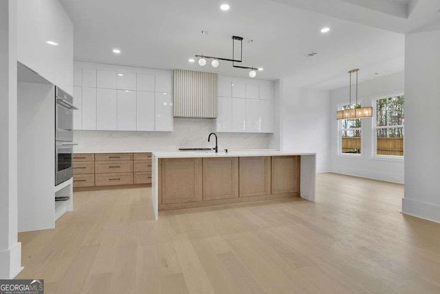 kitchen featuring white cabinetry, an island with sink, hanging light fixtures, and light hardwood / wood-style flooring