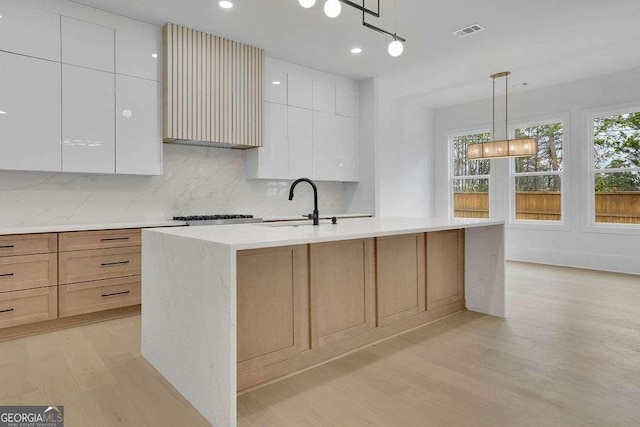 kitchen featuring white cabinetry, tasteful backsplash, light hardwood / wood-style floors, a center island with sink, and decorative light fixtures