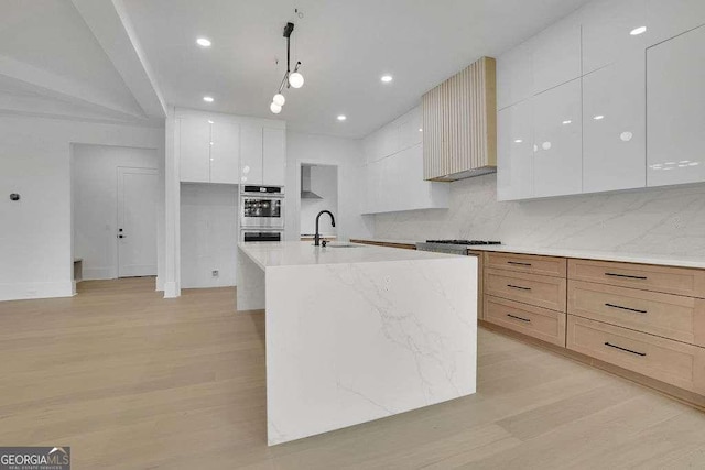 kitchen featuring sink, white cabinetry, hanging light fixtures, a kitchen island with sink, and light brown cabinets