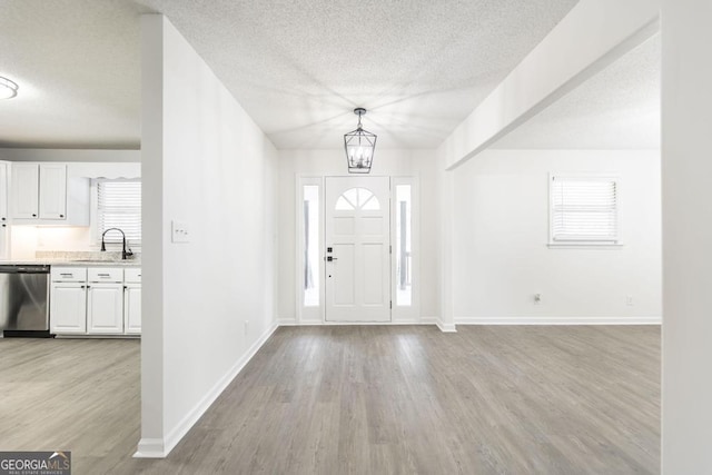 entrance foyer with a notable chandelier, sink, a textured ceiling, and light wood-type flooring