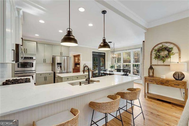 kitchen with appliances with stainless steel finishes, a breakfast bar, pendant lighting, sink, and ornamental molding