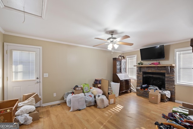 living room with a stone fireplace, ornamental molding, ceiling fan, and light wood-type flooring