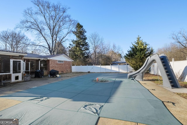 view of pool with a water slide, a patio area, and a sunroom