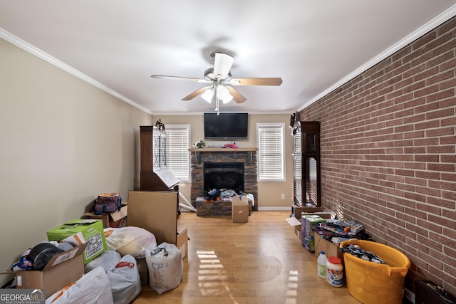 living room featuring ceiling fan, ornamental molding, brick wall, a stone fireplace, and light wood-type flooring