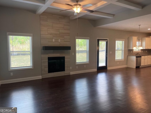 unfurnished living room featuring plenty of natural light, coffered ceiling, a tiled fireplace, and beam ceiling