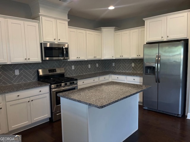 kitchen with stainless steel appliances, white cabinetry, dark stone countertops, and decorative backsplash