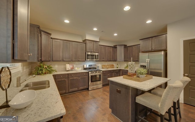 kitchen featuring sink, a kitchen breakfast bar, a kitchen island, stainless steel appliances, and light stone countertops