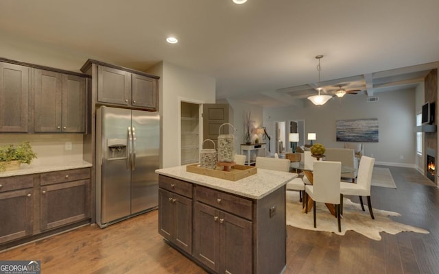 kitchen with dark brown cabinetry, stainless steel refrigerator with ice dispenser, a center island, and light stone counters