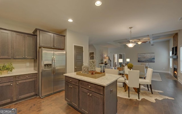 kitchen featuring stainless steel refrigerator with ice dispenser, light stone counters, decorative light fixtures, a center island, and dark hardwood / wood-style flooring