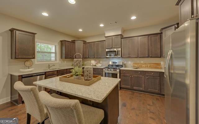 kitchen with a kitchen island, sink, dark hardwood / wood-style flooring, stainless steel appliances, and light stone countertops