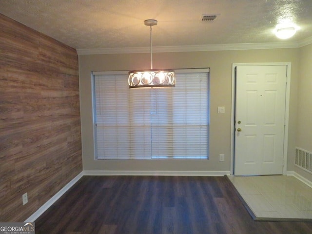 unfurnished dining area featuring dark wood-type flooring, ornamental molding, a textured ceiling, and wood walls