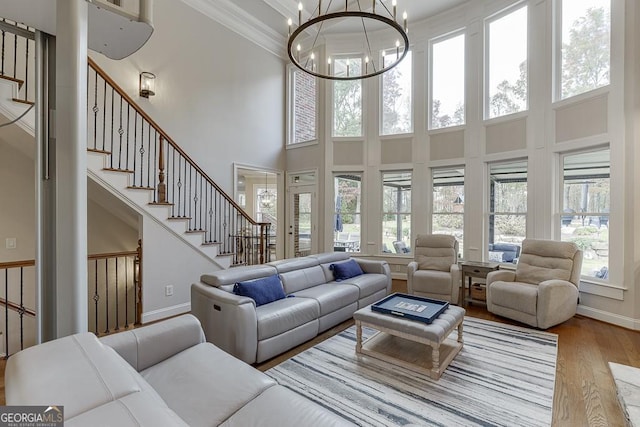 living room with crown molding, a towering ceiling, a chandelier, and light hardwood / wood-style floors